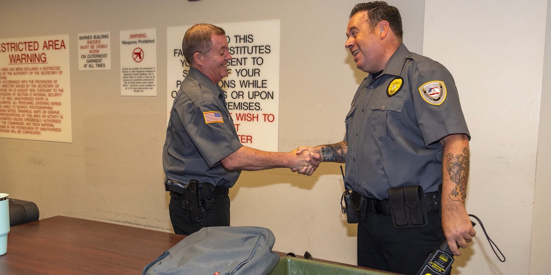 Two Securemedy officers in grey uniforms shaking hands at a screening checkpoint