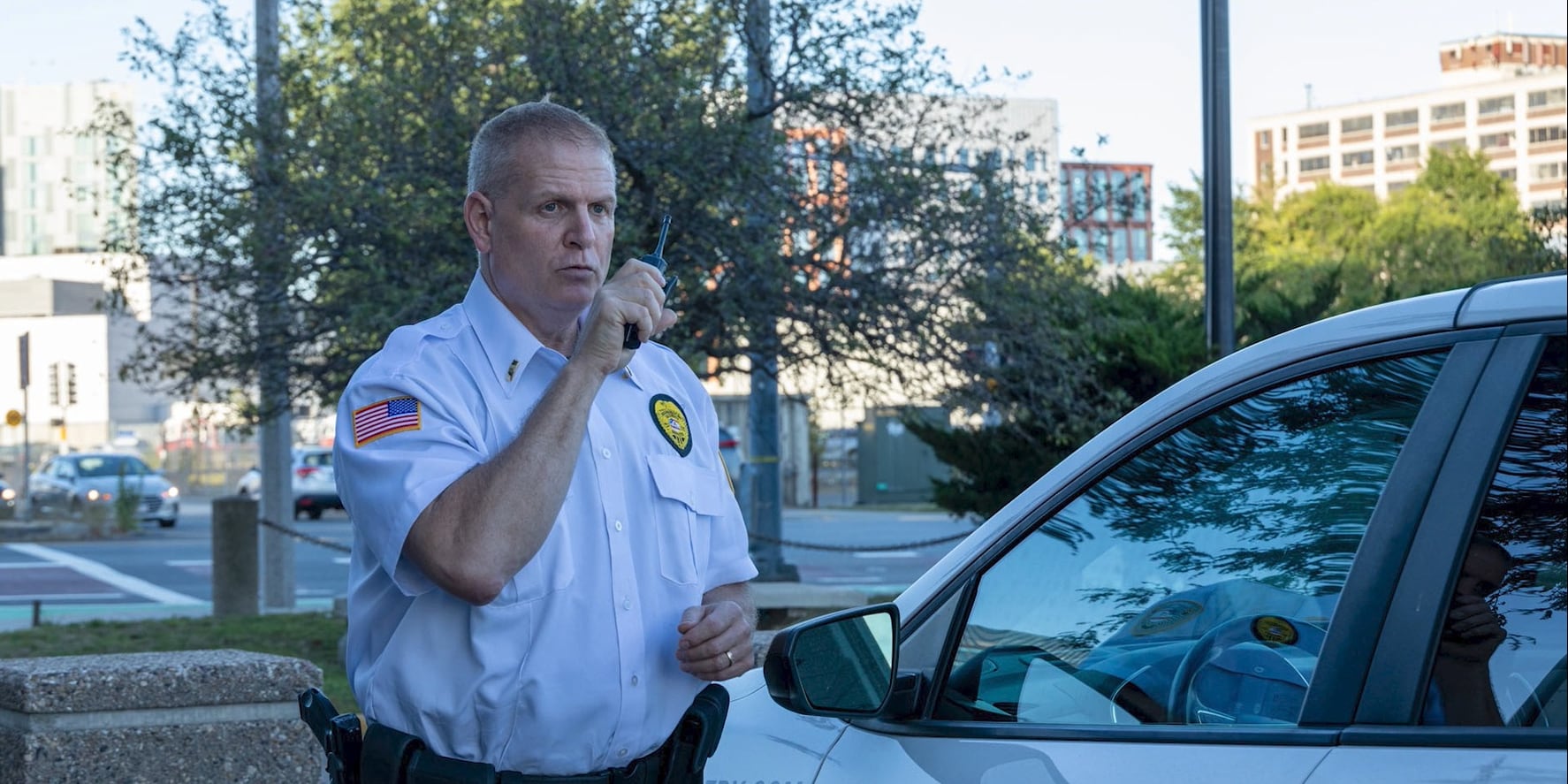Securemedy supervisor in a white uniform communicating by radio beside a patrol vehicle