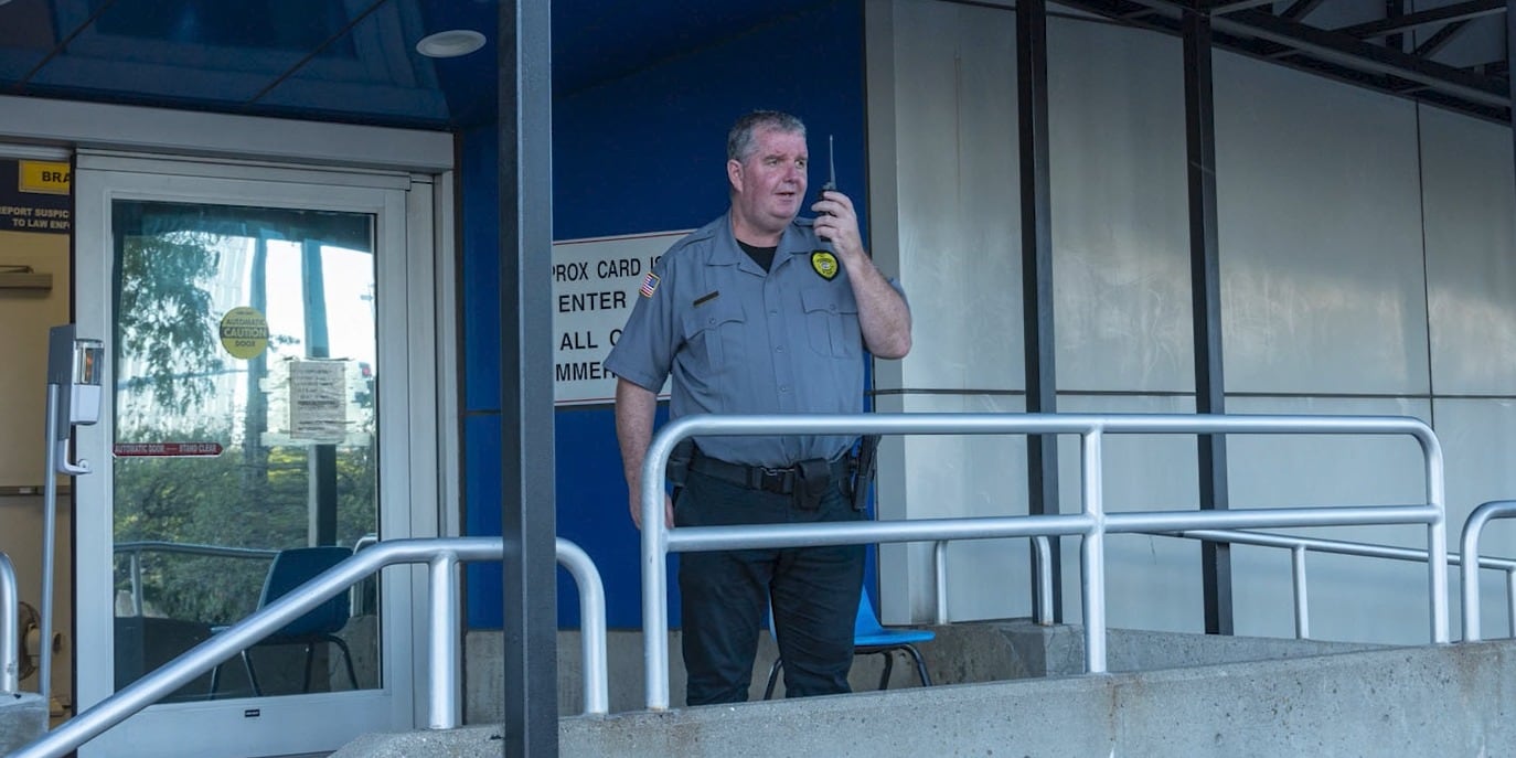 Securemedy officer in a grey uniform using a radio at a building entrance