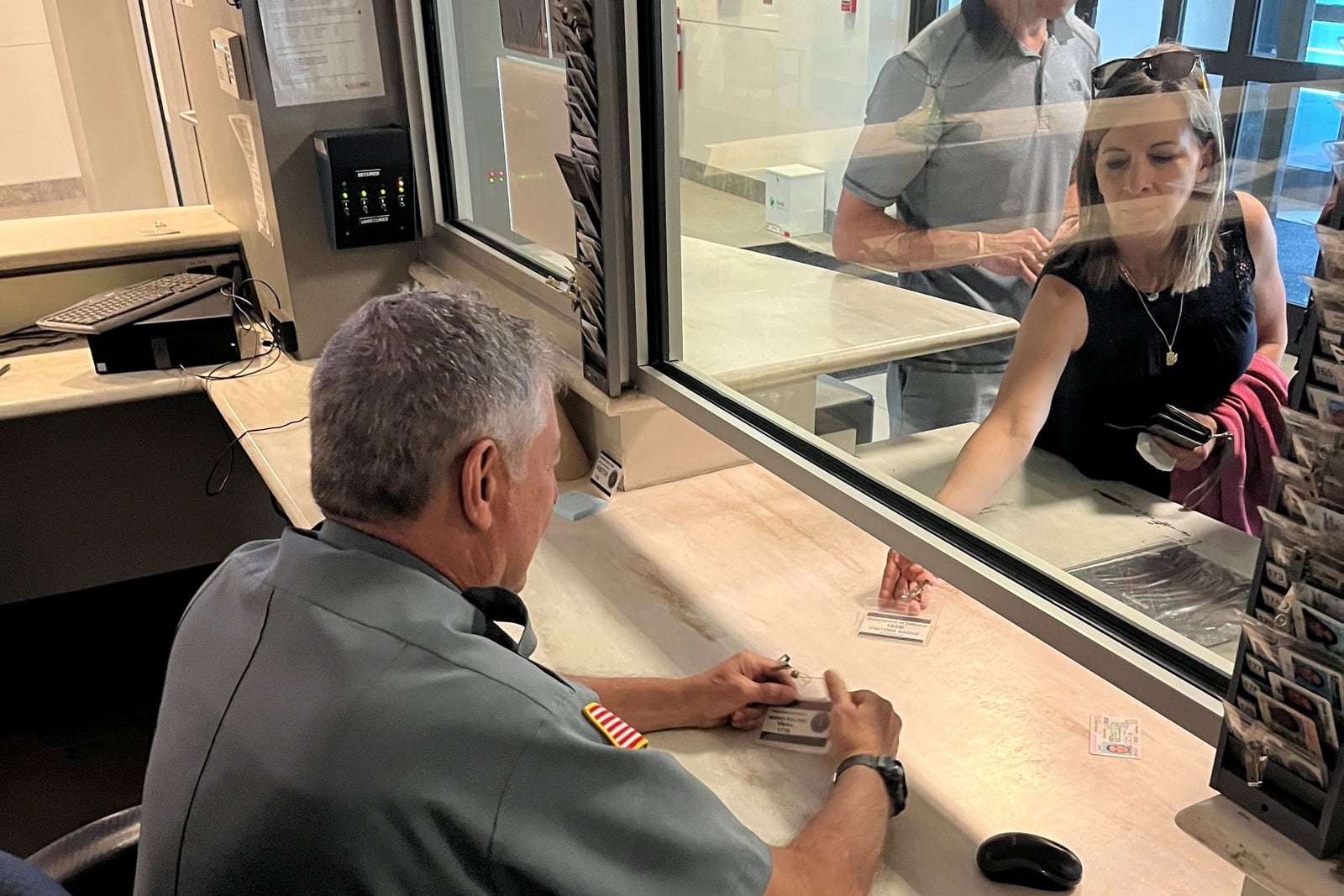 Securemedy officer in a grey uniform checking visitor identification at a reception window