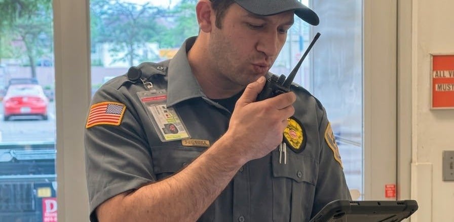 Securemedy officer in a grey uniform using a radio and a tablet
