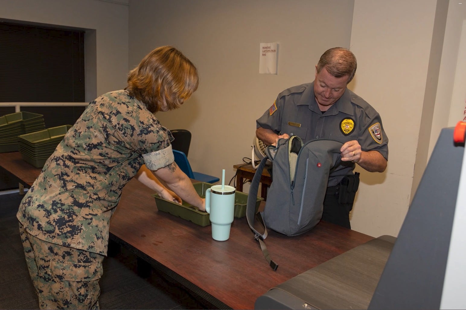 Securemedy officer in a grey uniform inspecting a bag at a building screening checkpoint